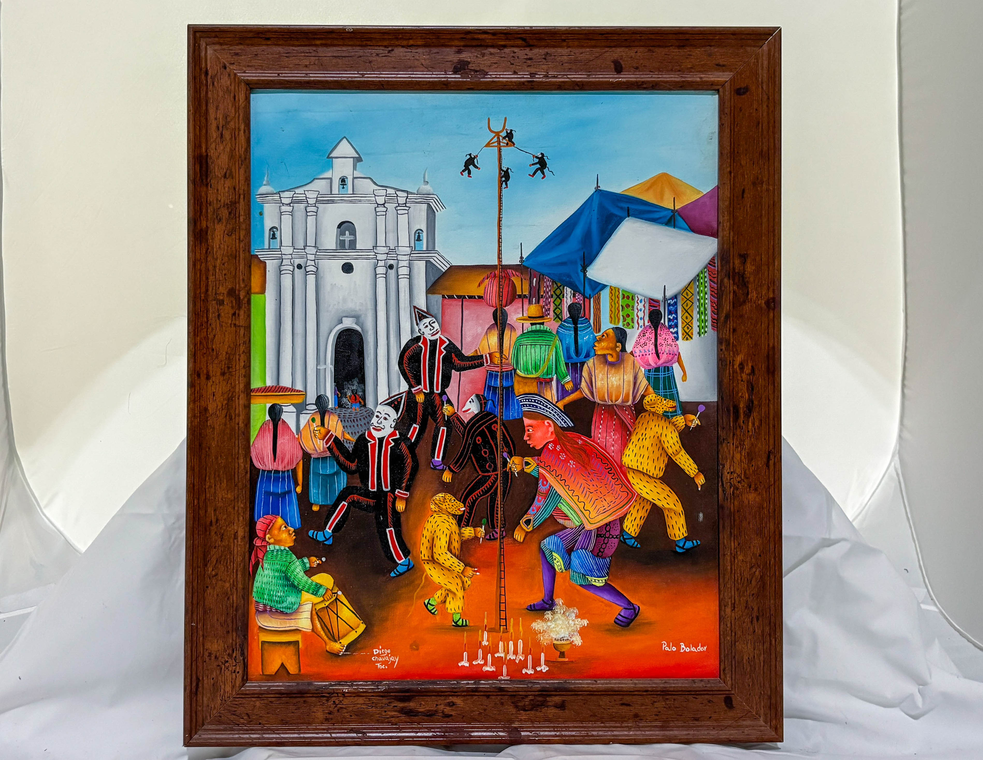 Framed colorful painting of a lively street scene with people and buildings.